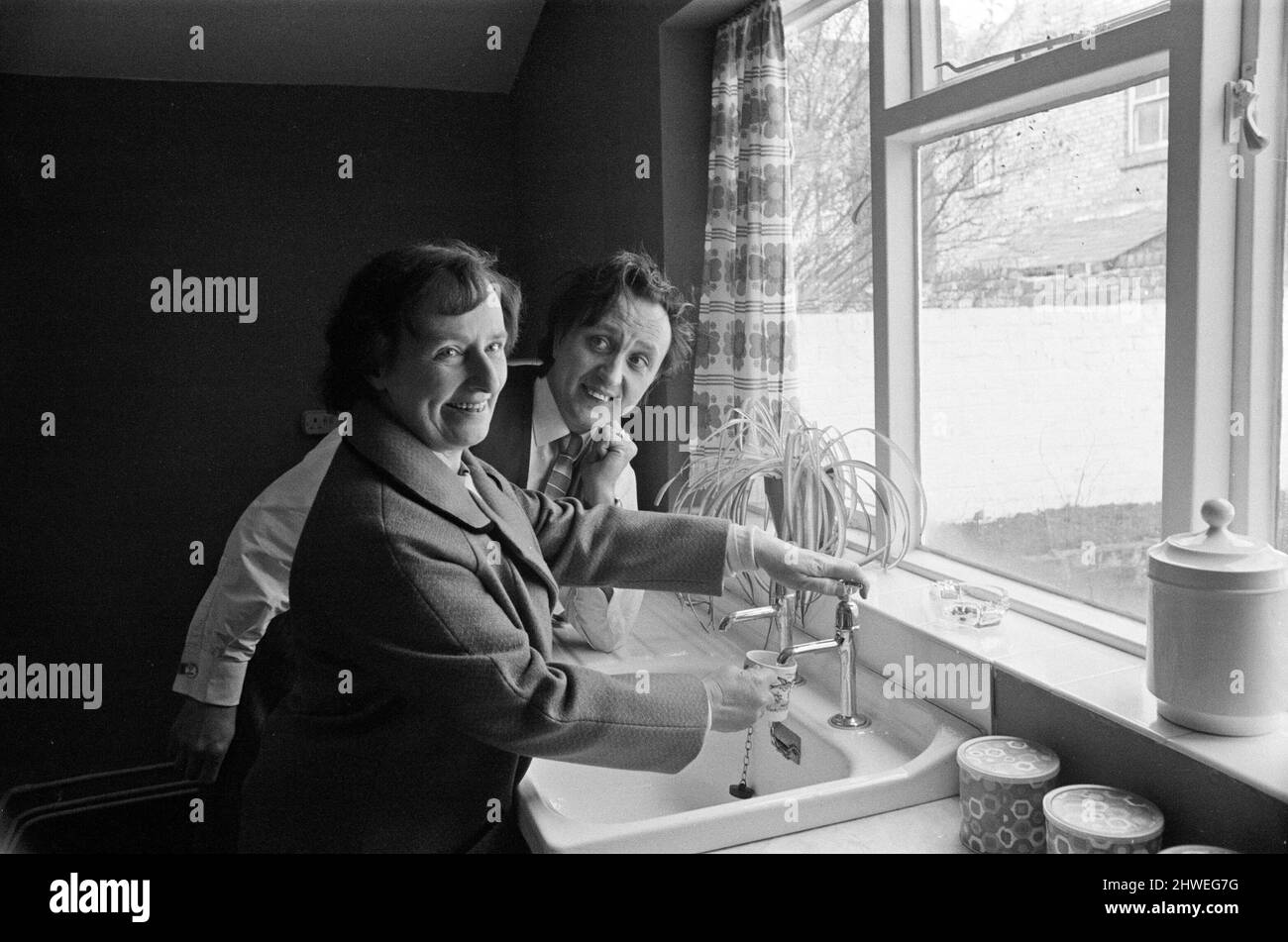 Le comédien Ken Dodd ouvre des appartements à Ducie Street et Beaconsfield Street, Toxteth, Liverpool. Deux maisons, une dans chaque rue, ont été converties en appartements sous la direction d'une équipe d'experts en logement et en planification. Ken boit une tasse d'eau dans la nouvelle cuisine de Mme Margaret Gibbs, rue Ducie. 7th avril 1970. Banque D'Images