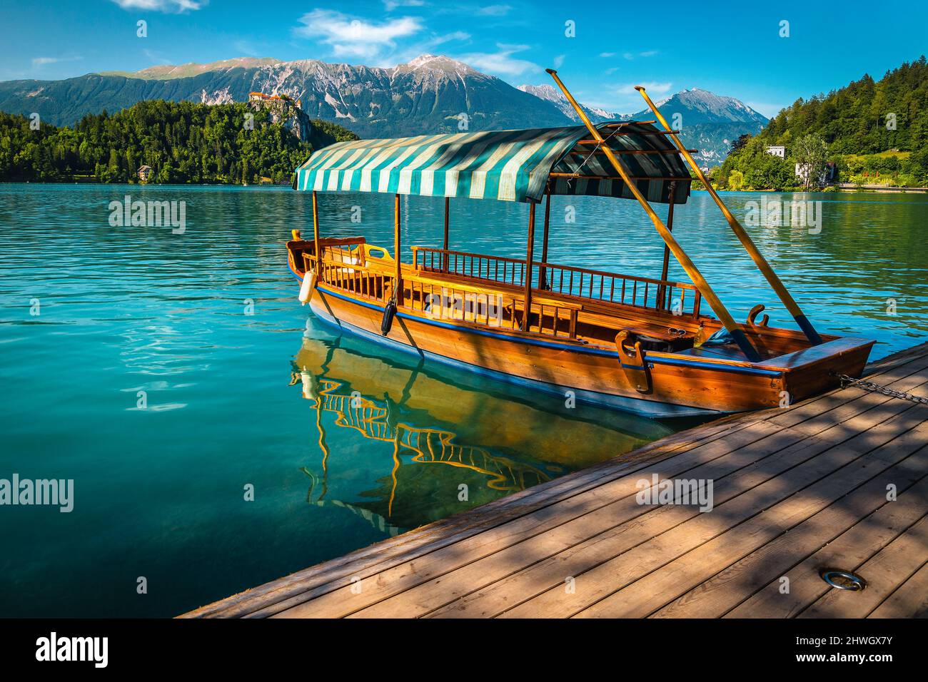 Bateau touristique traditionnel à rames en bois de Pletna ancré à la jetée. Bateau en bois de Pletna sur le célèbre lac de Bled et château médiéval sur la colline de ba Banque D'Images