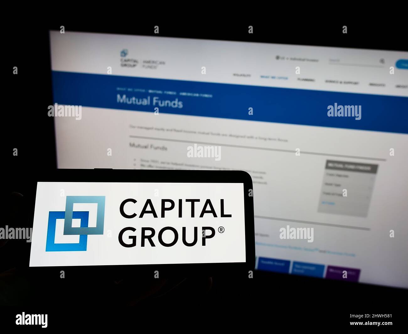 Personne tenant un téléphone portable avec le logo de la société financière américaine Capital Group Companies Inc. À l'écran en face de la page Web. Mise au point sur l'affichage du téléphone. Banque D'Images