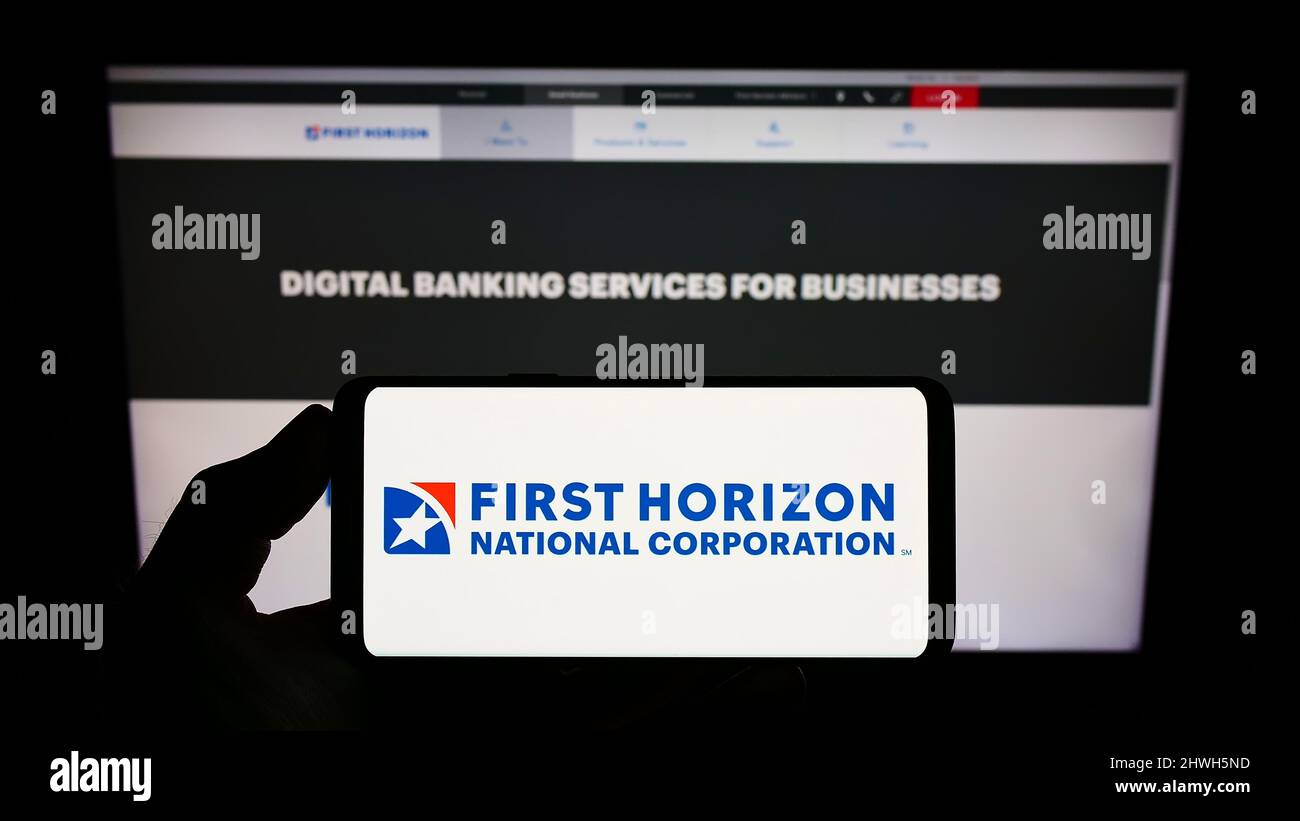 Personne détenant un smartphone avec le logo de la société américaine First Horizon Corporation (FHN) à l'écran devant le site Web. Mise au point sur l'affichage du téléphone. Banque D'Images