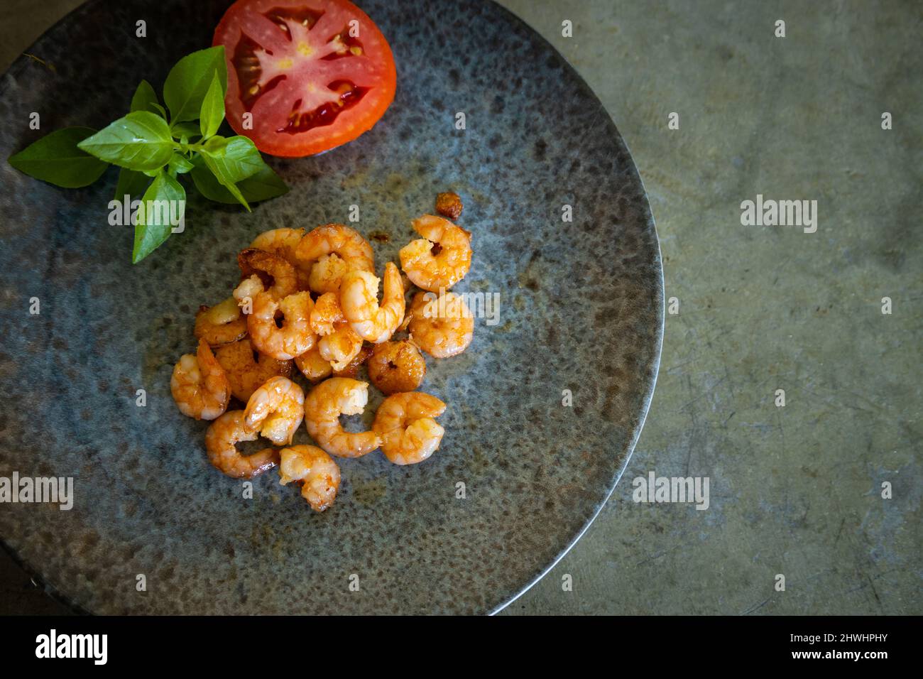 De délicieuses crevettes fraîchement cuites sur une assiette grise à côté d'une tomate et d'un basilic. Espace libre à écrire. Fond gris neutre. Banque D'Images