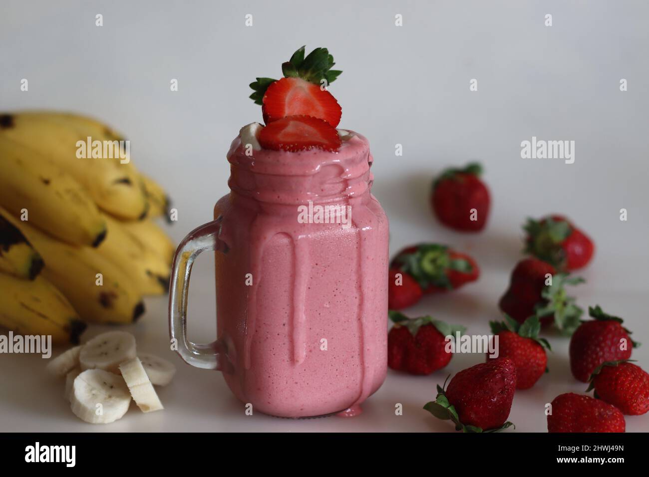 Smoothie fait de fraises fraîches, de banane et de lait d'amande. Servi dans un pot de maçon. Tourné sur fond blanc avec des bananes et des fraises. Banque D'Images