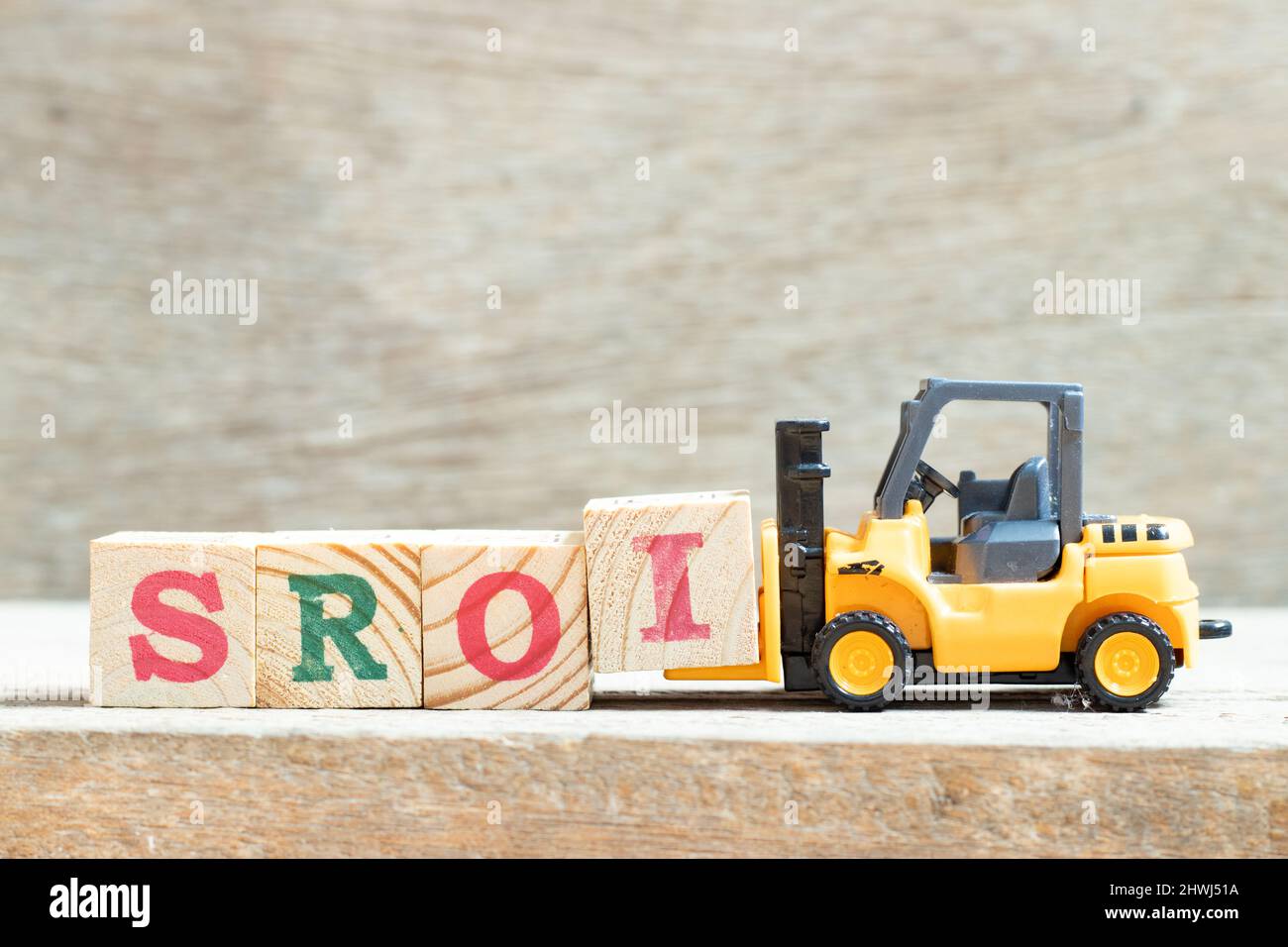 Chariot élévateur à jouets tenir le bloc de lettres I pour compléter le mot SROI (abréviation du retour sur investissement social) sur fond de bois Banque D'Images