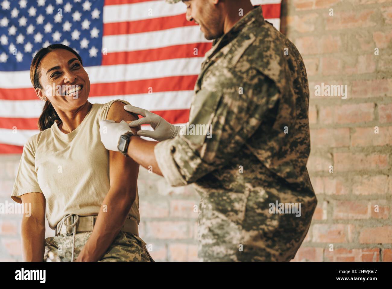 Une femme soldat sourit insouciante à l'infirmière militaire après avoir reçu un rappel de vaccin Covid-19. Militaire américaine ayant un adhésif médical Banque D'Images