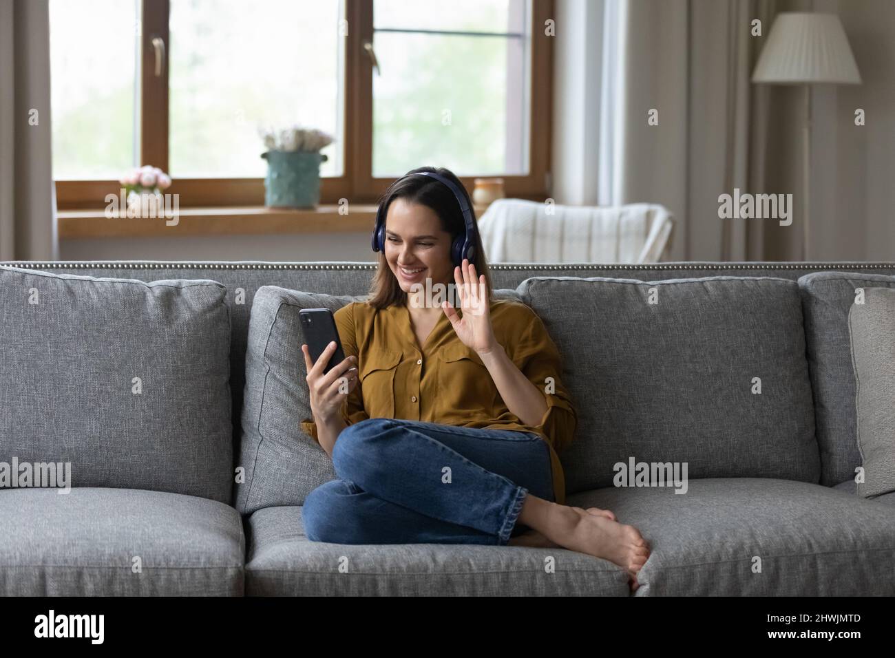 Une jeune femme s'assoit sur un canapé confortable tient un téléphone portable pour créer un vidéocall Banque D'Images