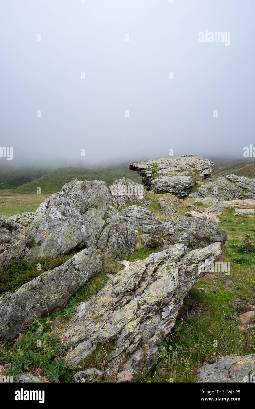 paysage de haute montagne avec des roches granitiques avec des lichens en premier plan et une épaisse banque de brouillard couvrant les montagnes en arrière-plan, vertical Banque D'Images
