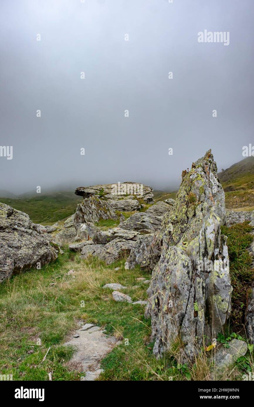 paysage de haute montagne avec des roches granitiques couvrant de lichens en premier plan et une épaisse banque de brouillard couvrant les montagnes en arrière-plan, verti Banque D'Images
