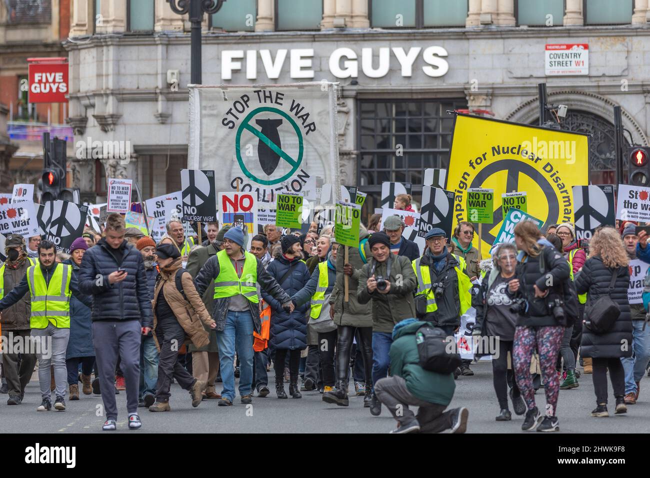 Londres, Royaume-Uni. 6 mars 2022. Une foule nombreuse se rassemble devant un restaurant Five Guys dans le centre de Londres lors d'une manifestation anti-guerre organisée par la Coalition Stop the War et la campagne pour le désarmement nucléaire. Les manifestants portent des gilets de sécurité jaunes et portent des pancartes avec des symboles de paix et des slogans tels que « NON À LA GUERRE » et « STOP THE WAR COALITION ». Arrêtez la guerre en Ukraine et ne marchez plus de protestation contre l'expansion de l'OTAN de la BBC à Trafalgar Square. Penelope Barritt/Alamy Live News Banque D'Images