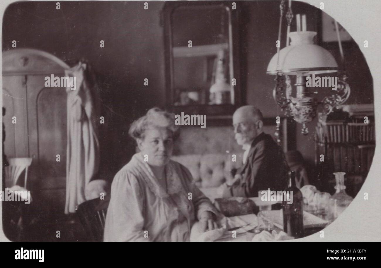 photographie antique d'un couple âgé (mari et femme) comme ils sont assis dans eux beau salon dans leur belle maison. Ils ont un miroir massif à l'arrière et un lustre néo baroque richement décoré dans le côté droit de l'image une grande armoire (avec une robe est accrochée dessus) sur le côté gauche de l'image. il y a une grande bouteille en verre (vin ou eau minérale) sur le bureau juste à côté de la dame. Belle maison. période : années 1900, source : photographie originale. . INFO-AUTORISATION-DROITS-SUPPLÉMENTAIRES-NON-DISPONIBLE / collectionneur d'œuvres d'art et maison Banque D'Images