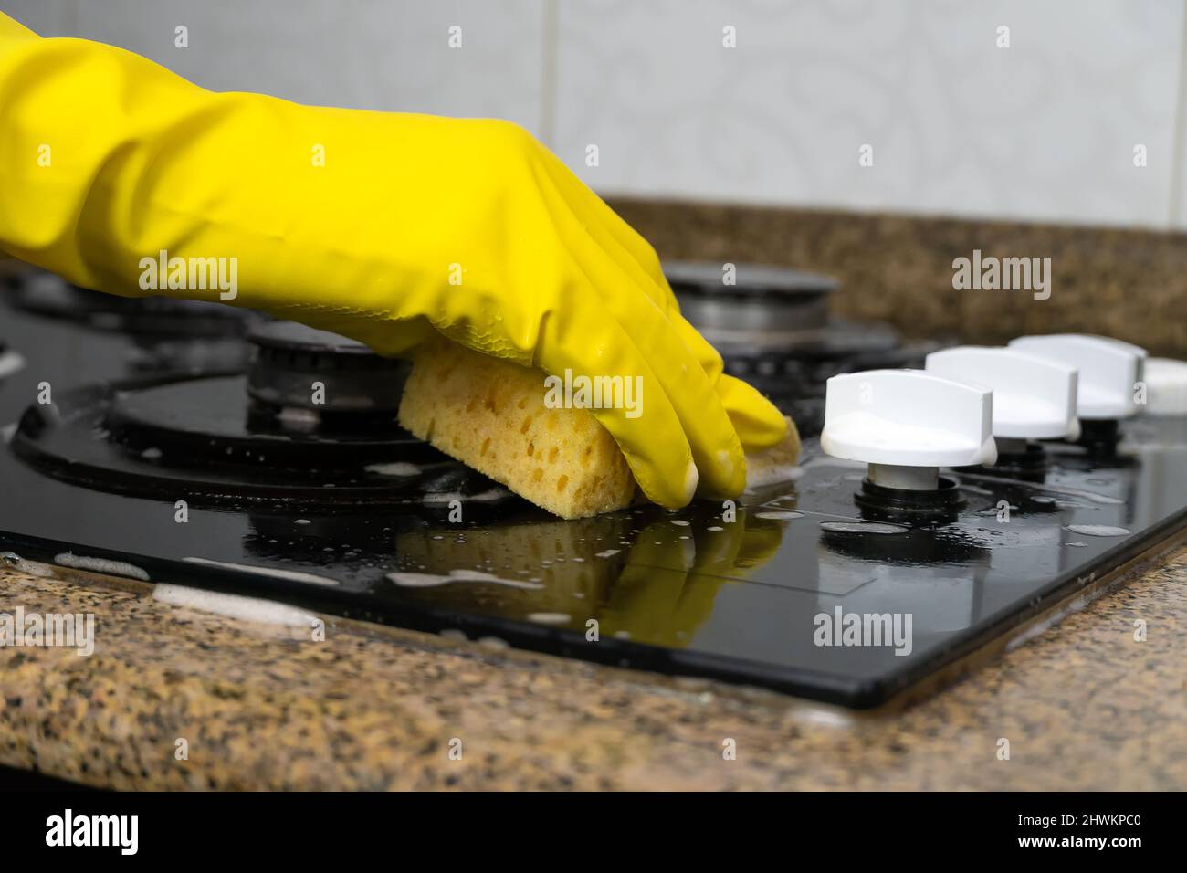 Gros plan de la main d'une femme en gants jaunes, lavage de la cuisinière avec un agent nettoyant et une éponge Banque D'Images