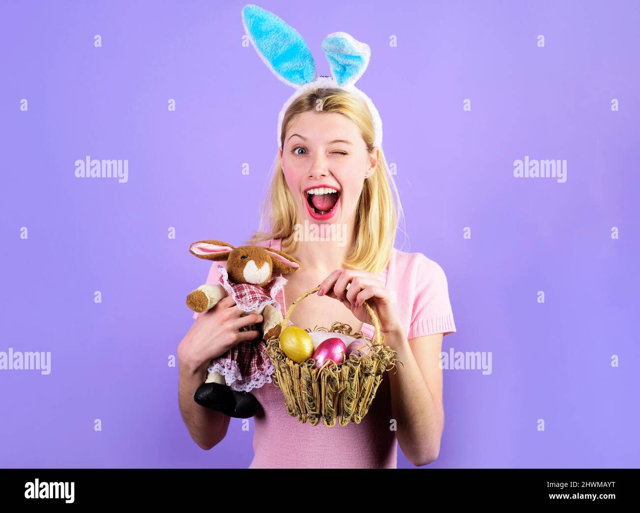 Le jour de Pâques. Une jeune fille qui se fait entortiller avec un panier d'œufs de couleur et un jouet de lapin en peluche. Bonne femme dans les oreilles de lapin. Banque D'Images