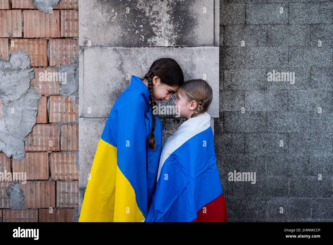 Petites filles avec des drapeaux ukrainiens et russes devant un mur détruit par des bombes. Ukraine russie conflit 2022 escalade. Concept de paix Banque D'Images