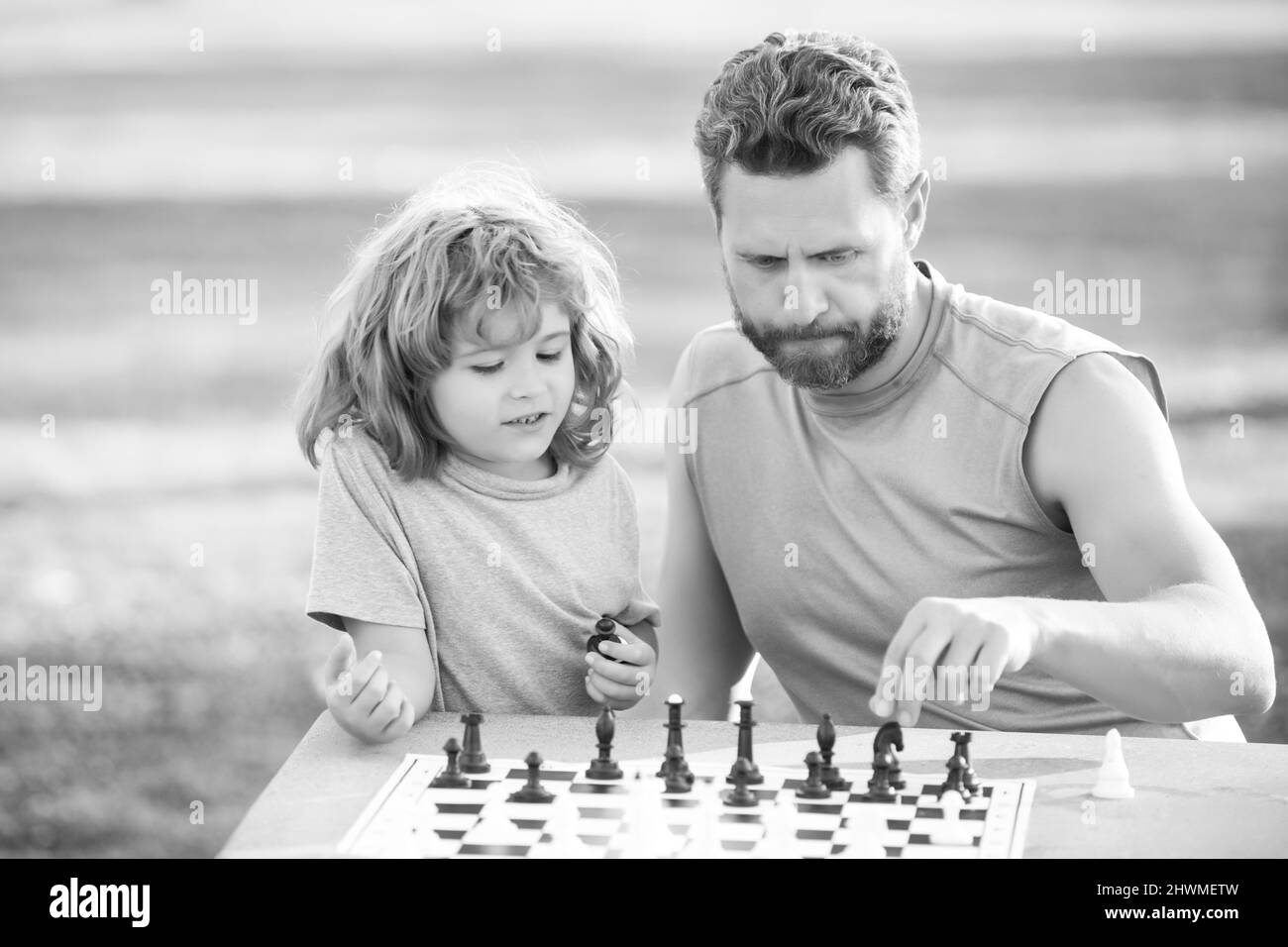 Fils se posant sur l'herbe et jouant aux échecs avec le père. Enfant garçon concentré développant la stratégie d'échecs, jouant à un jeu de société avec parent. Jeux et Banque D'Images