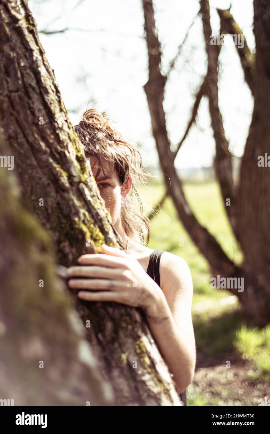 la femme naturelle regarde derrière le tronc d'arbre en mousse sous le soleil de l'après-midi Banque D'Images
