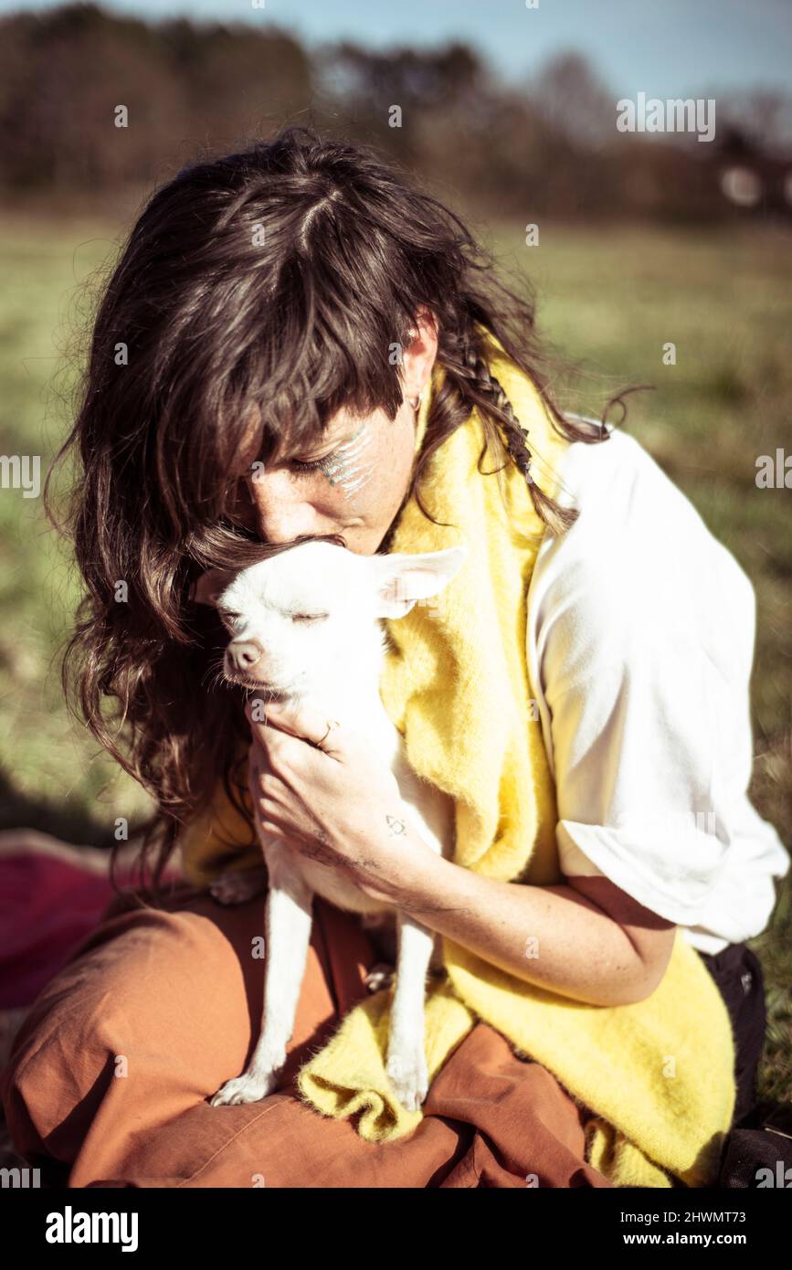 La jeune femme naturelle alternative embrasse un petit chien blanc sur l'herbe Banque D'Images