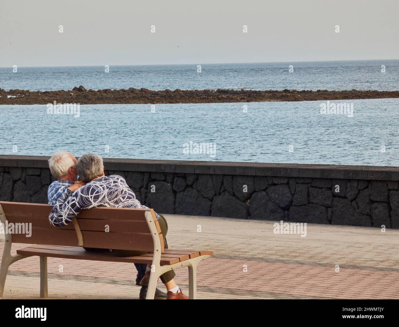 couple âgé assis sur un banc en face de la mer avec un masque Banque D'Images