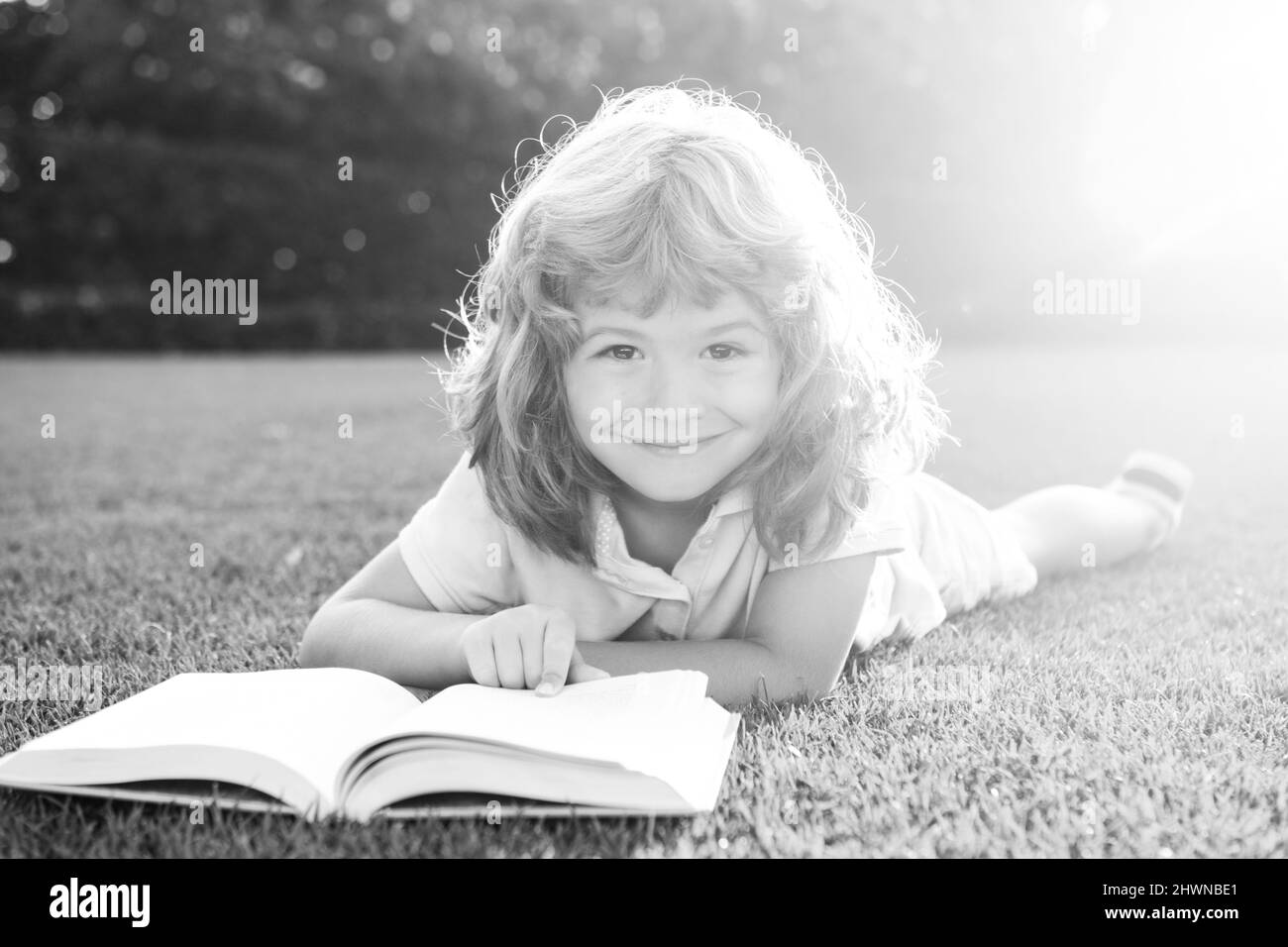 Enfant garçon lisant le livre d'intérêt dans le jardin. L'été s'amuser. Adorable garçon allongé sur l'herbe lisant un livre pour enfants. Banque D'Images