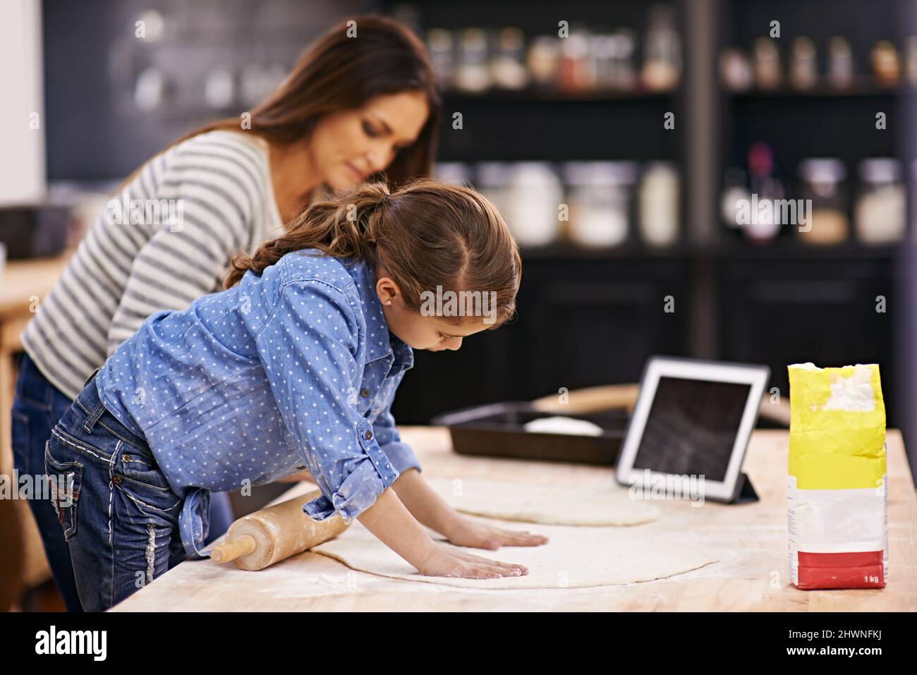 Pizzas faites maison à venir. Photo d'une mère et d'une fille qui cuit dans la cuisine avec une tablette numérique à côté. Banque D'Images