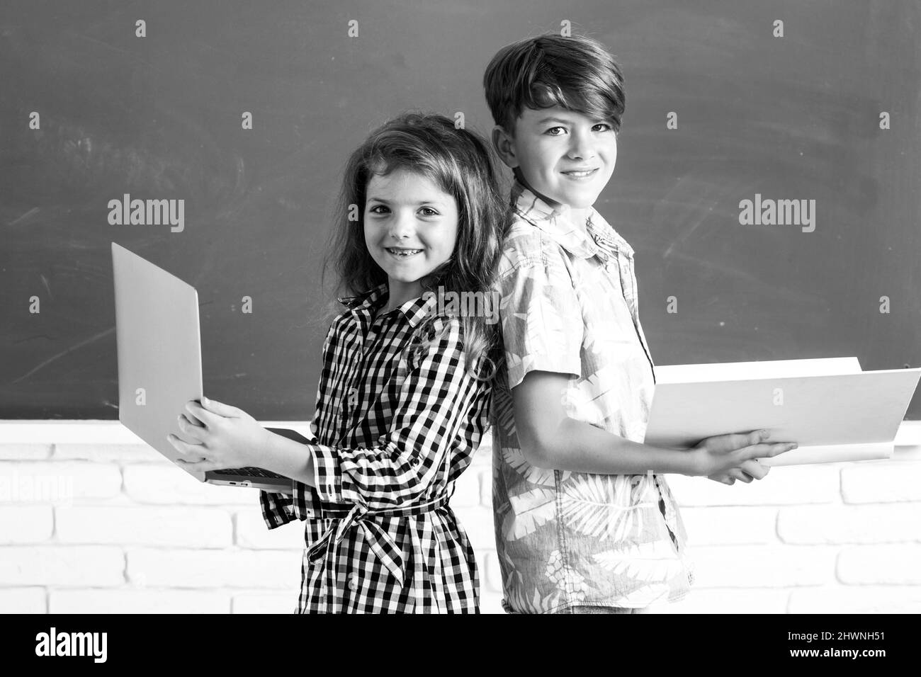 Les enfants de l'école primaire.Portrait d'enfants garçon et fille avec ordinateur portable et livre à l'école.Enfants en classe sur tableau noir. Banque D'Images