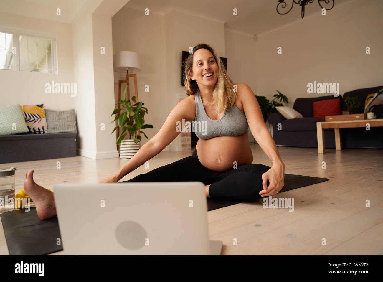 Souriant enceinte caucasienne femme souriant tout en s'étirant sur le tapis de yoga à la maison après le tutoriel de fitness en ligne Banque D'Images
