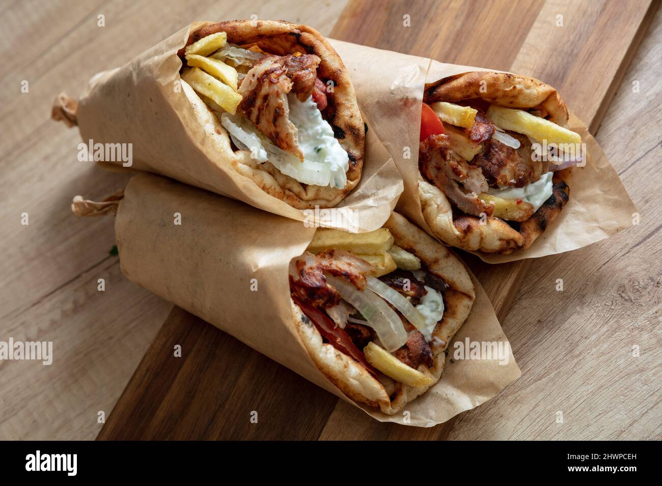 Shawarma Gyro pita sur une table en bois. Nourriture grecque, viande tranchée, pomme de terre, tomate et tzatziki, papier d'emballage, vue rapprochée. Banque D'Images