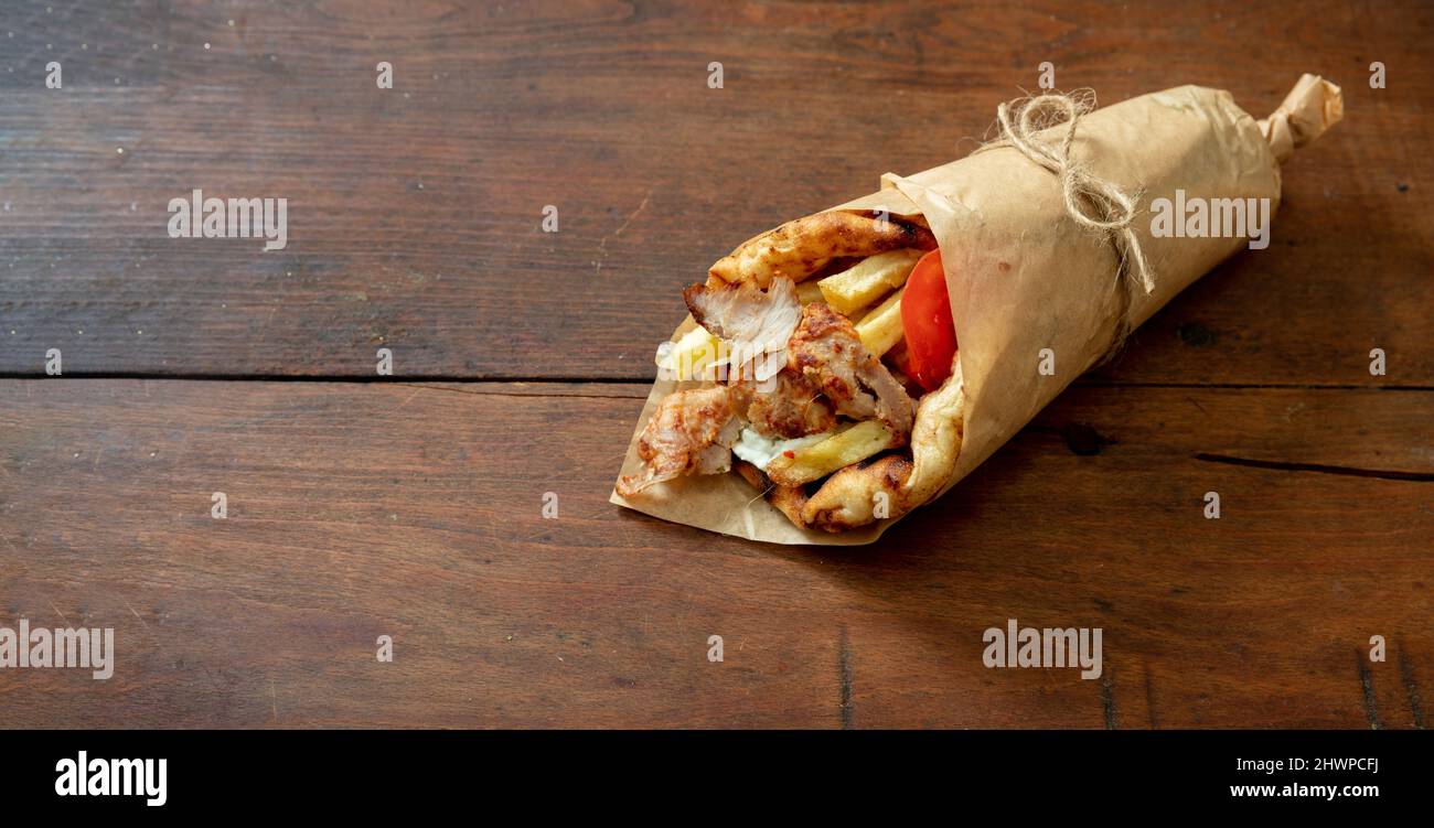 Gyro pita Shawarma sur une table en bois. Nourriture grecque, viande tranchée, pomme de terre, tomate et tzatziki, papier d'emballage, vue de dessus. Banque D'Images