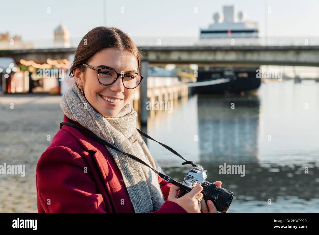 Jeune femme souriante avec caméra sur la rive par beau temps Banque D'Images