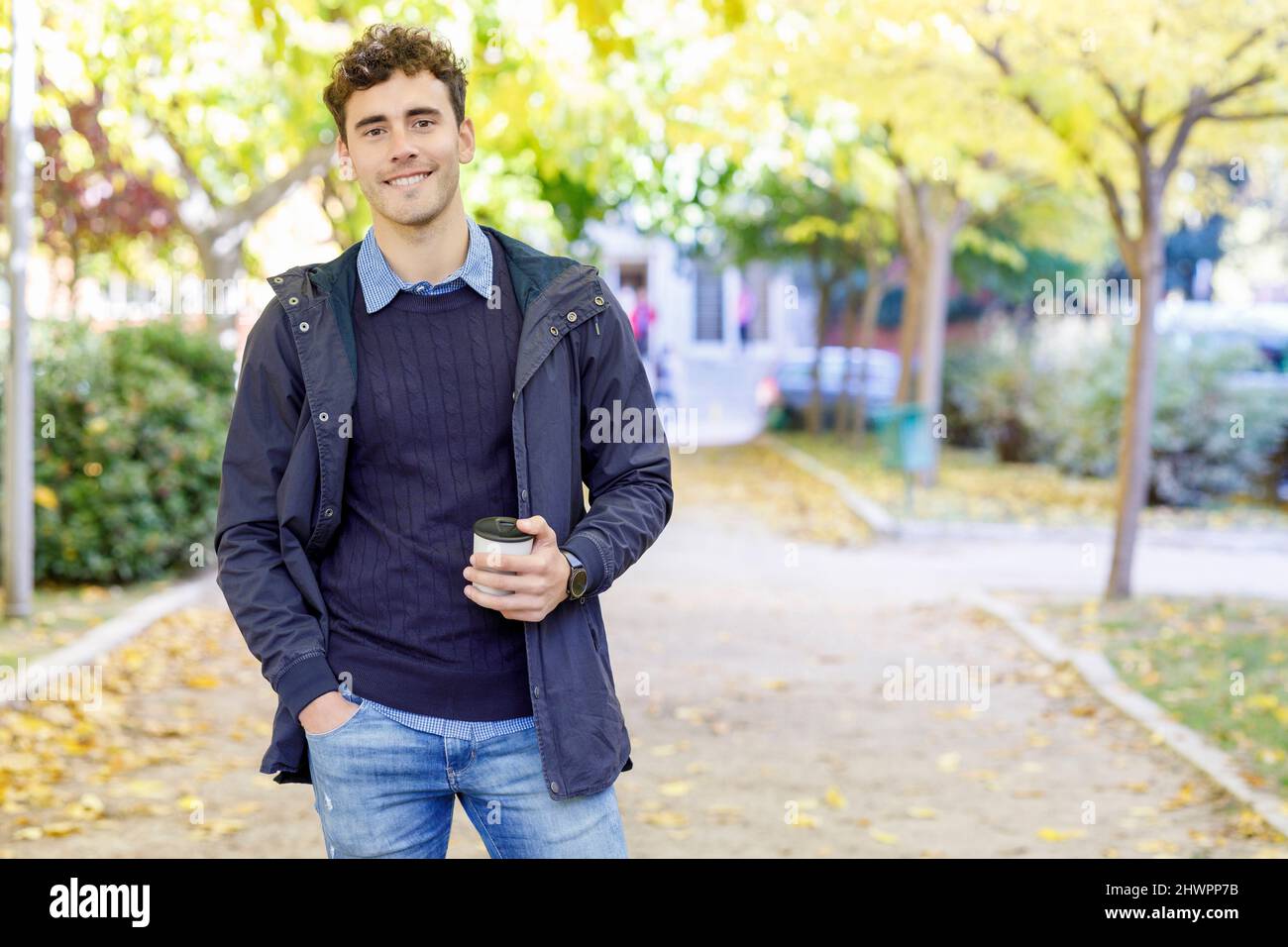 Homme souriant avec une tasse de café jetable dans le parc universitaire Banque D'Images