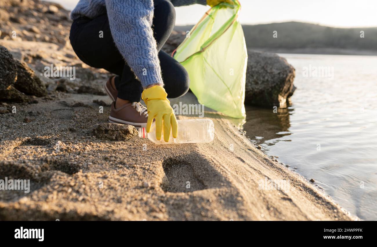 Femme ramassant une bouteille en plastique sur la plage en bord de mer Banque D'Images