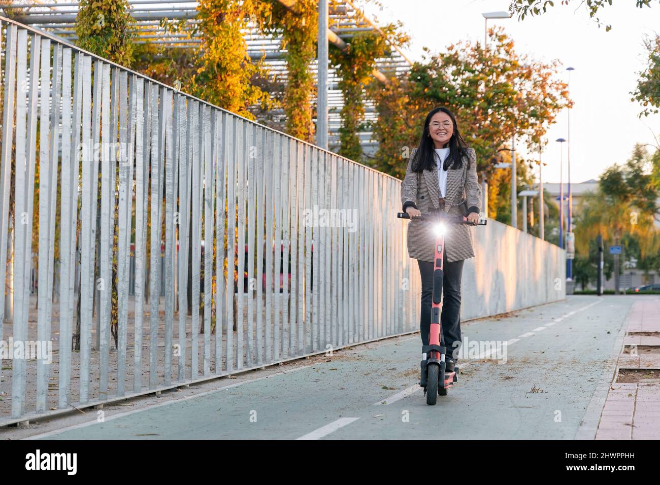 Femme d'affaires à bord d'un scooter électrique près d'une clôture sur une piste de marche Banque D'Images