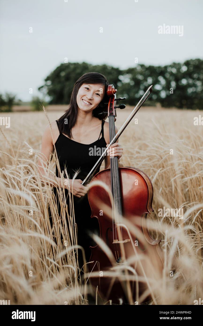 Femme souriante tenant le violoncelle au milieu des récoltes dans le champ Banque D'Images