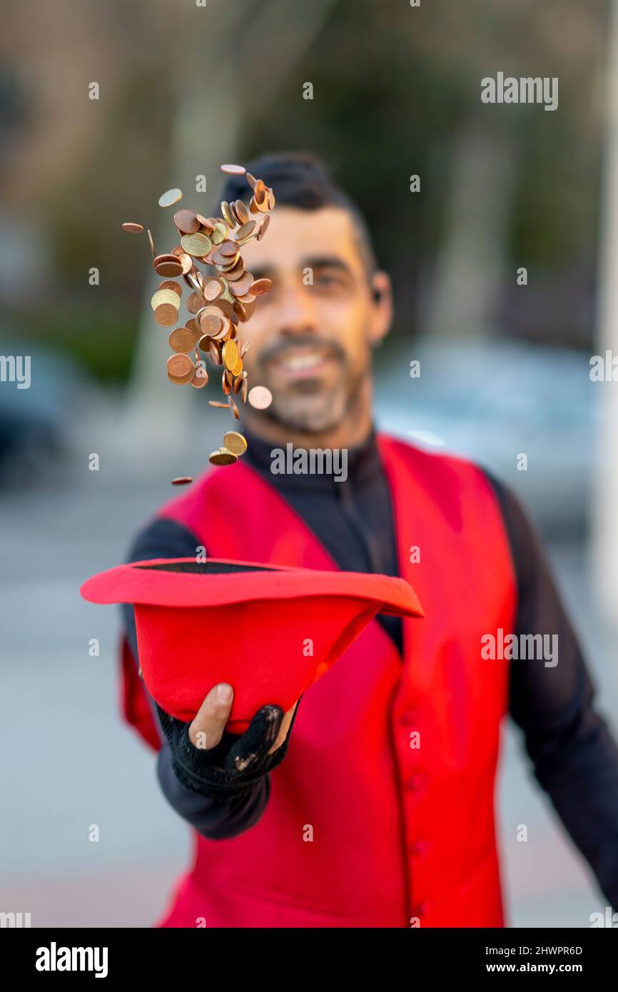 Un artiste de rue lance des pièces de monnaie à partir d'un chapeau rouge Banque D'Images