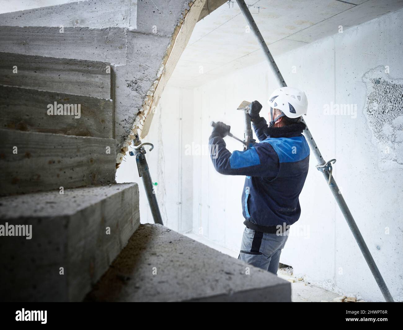 Ouvrier retirant les tuyaux des escaliers en béton sur le chantier de construction Banque D'Images