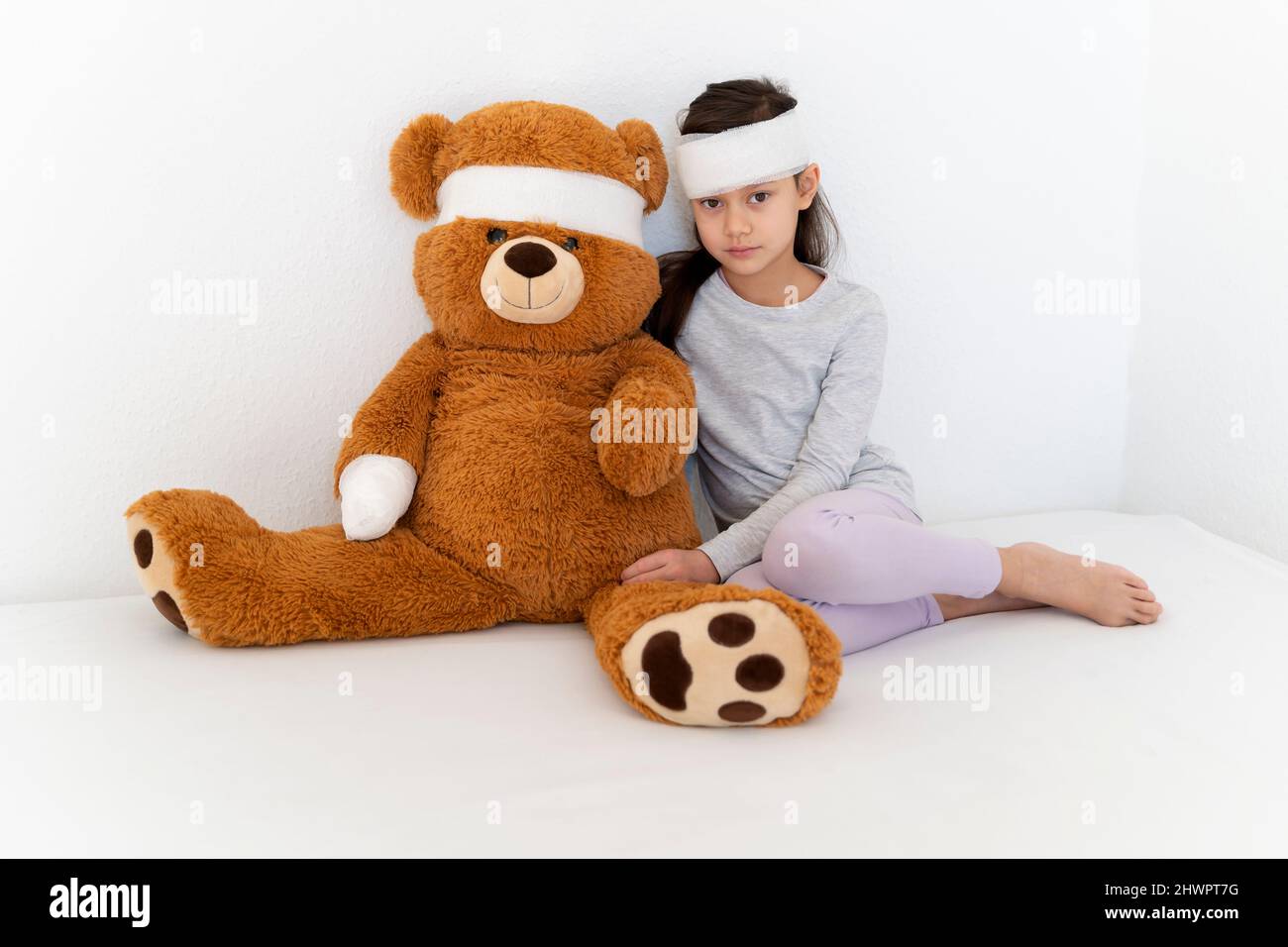 Bandage sur la fille avec l'ours en peluche assis devant le mur blanc Banque D'Images