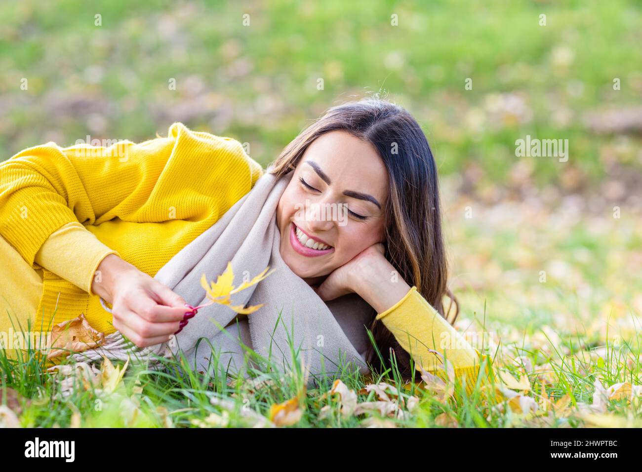 Jeune femme heureuse avec feuilles couchée sur l'herbe dans le parc d'automne Banque D'Images