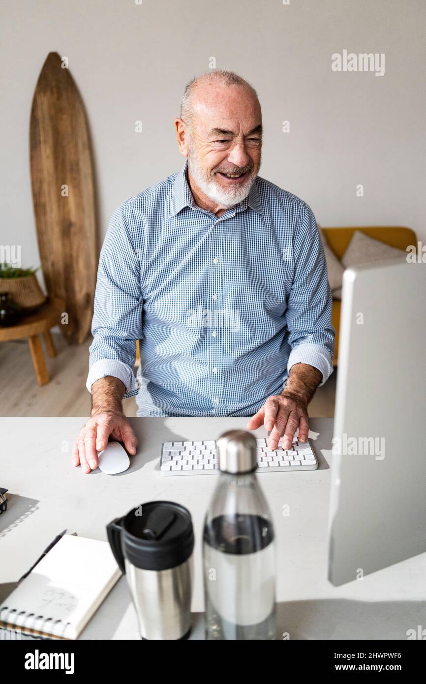 Homme d'affaires souriant utilisant un ordinateur au bureau à la maison Banque D'Images
