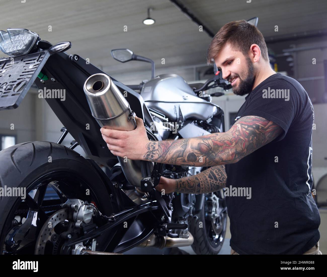 Un mécanicien tatoué examine le tuyau d'échappement de la moto en atelier Banque D'Images