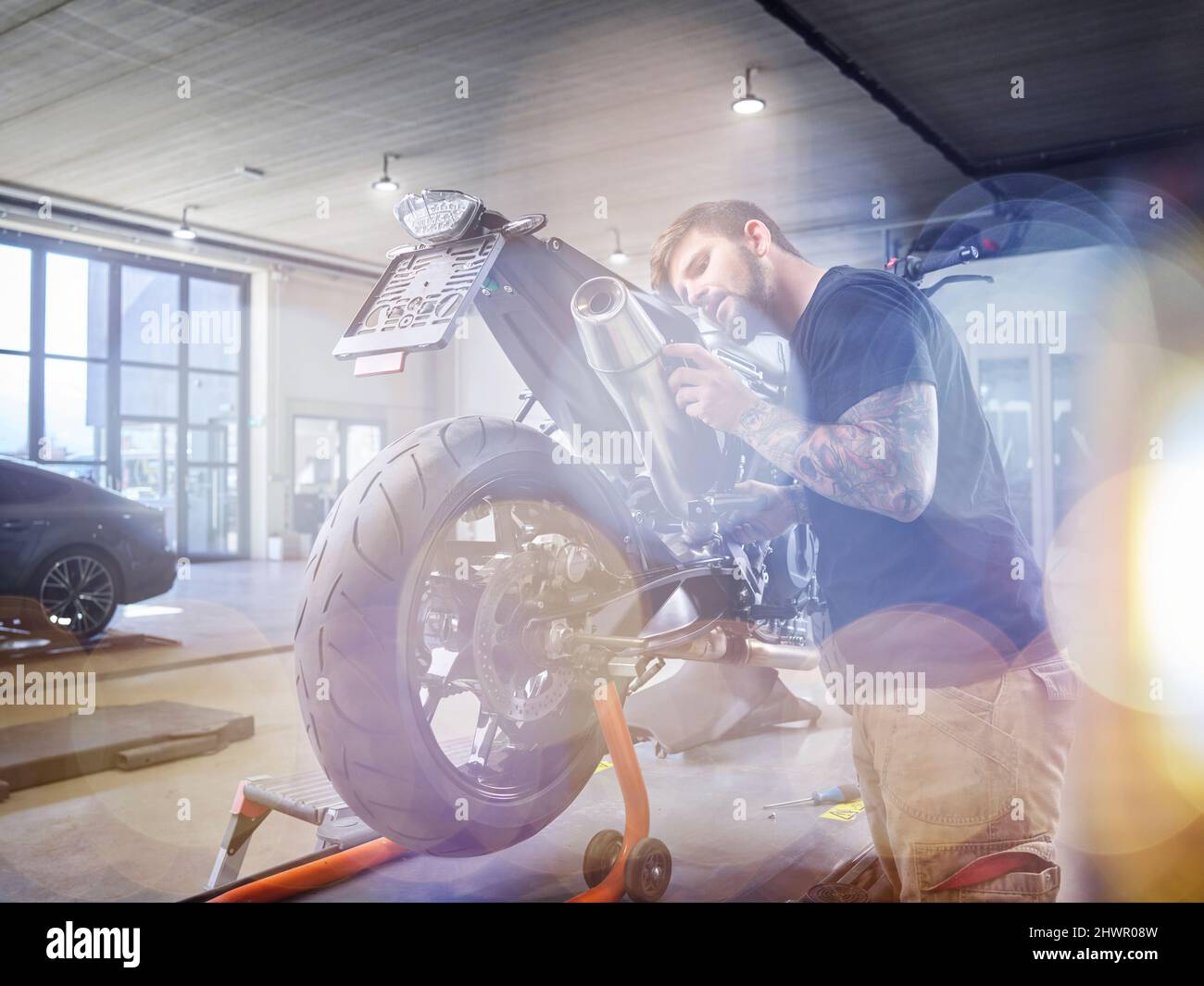 Jeune mécanicien examinant le tuyau d'échappement de la moto en atelier Banque D'Images