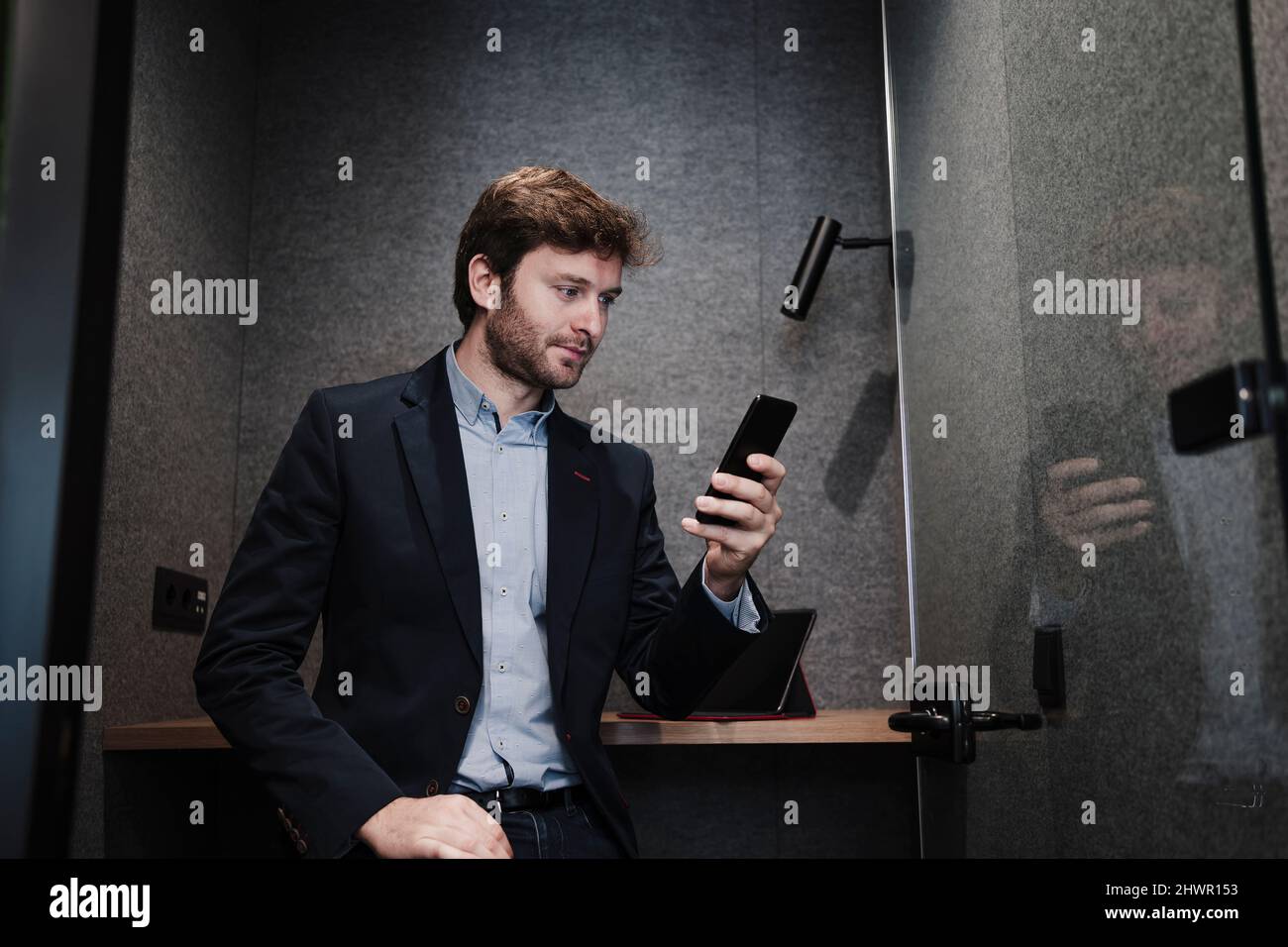 Homme d'affaires surfant sur un filet sur un téléphone portable, assis au bureau dans la cabine Banque D'Images