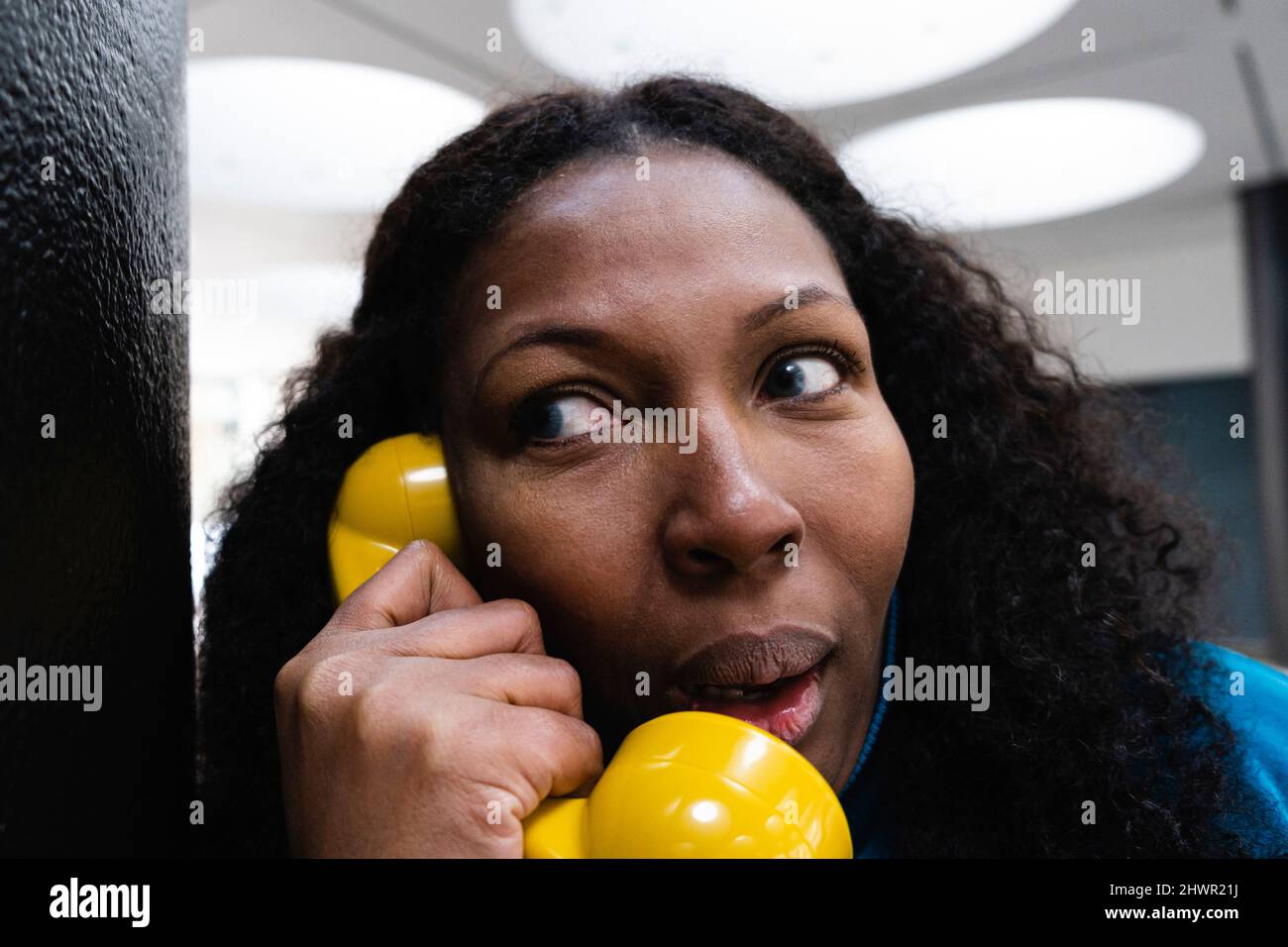 Curieuse femme à l'écoute à travers le vieux récepteur de téléphone jaune Banque D'Images