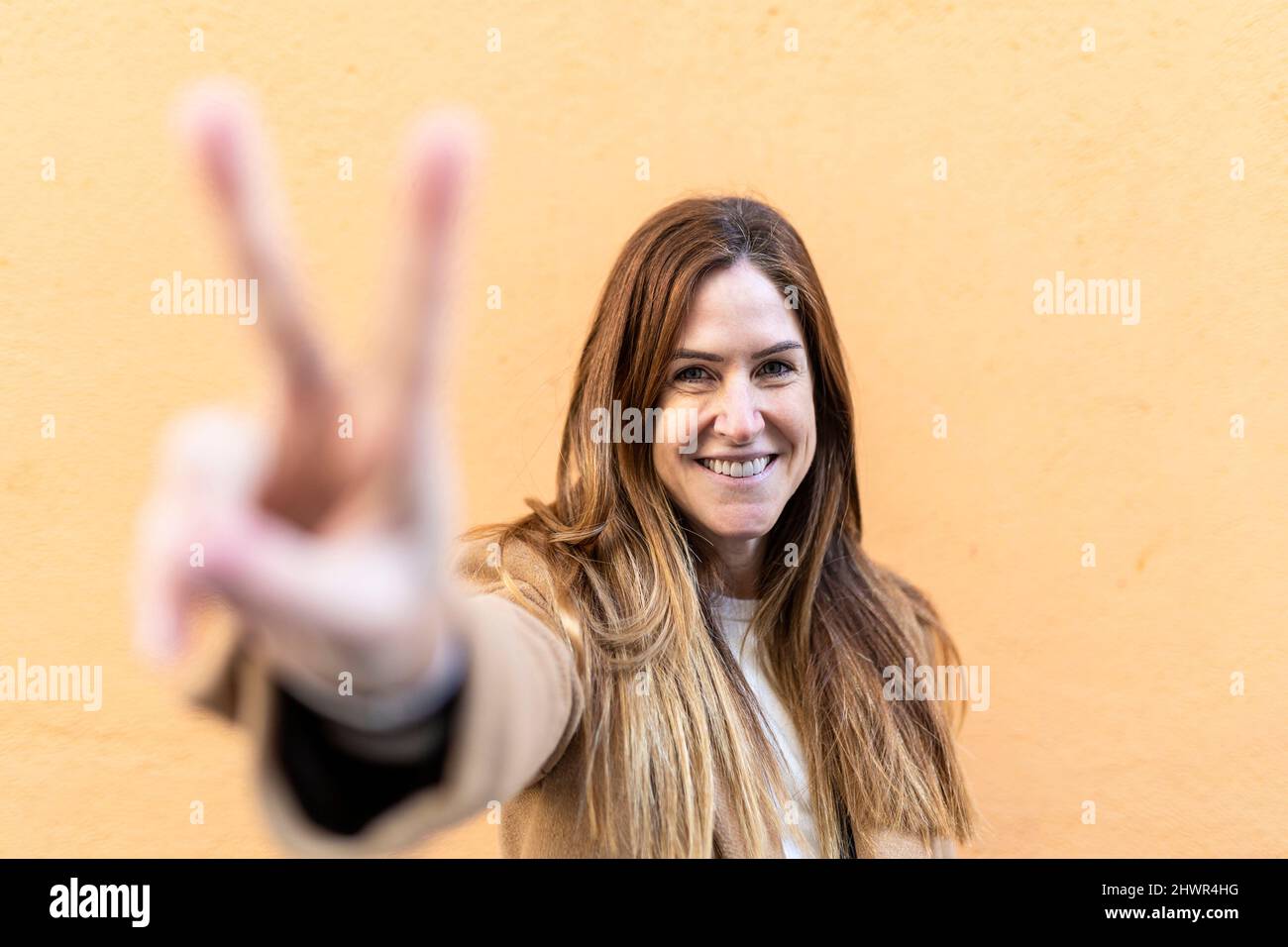 Femme souriante signe de paix devant le mur Banque D'Images
