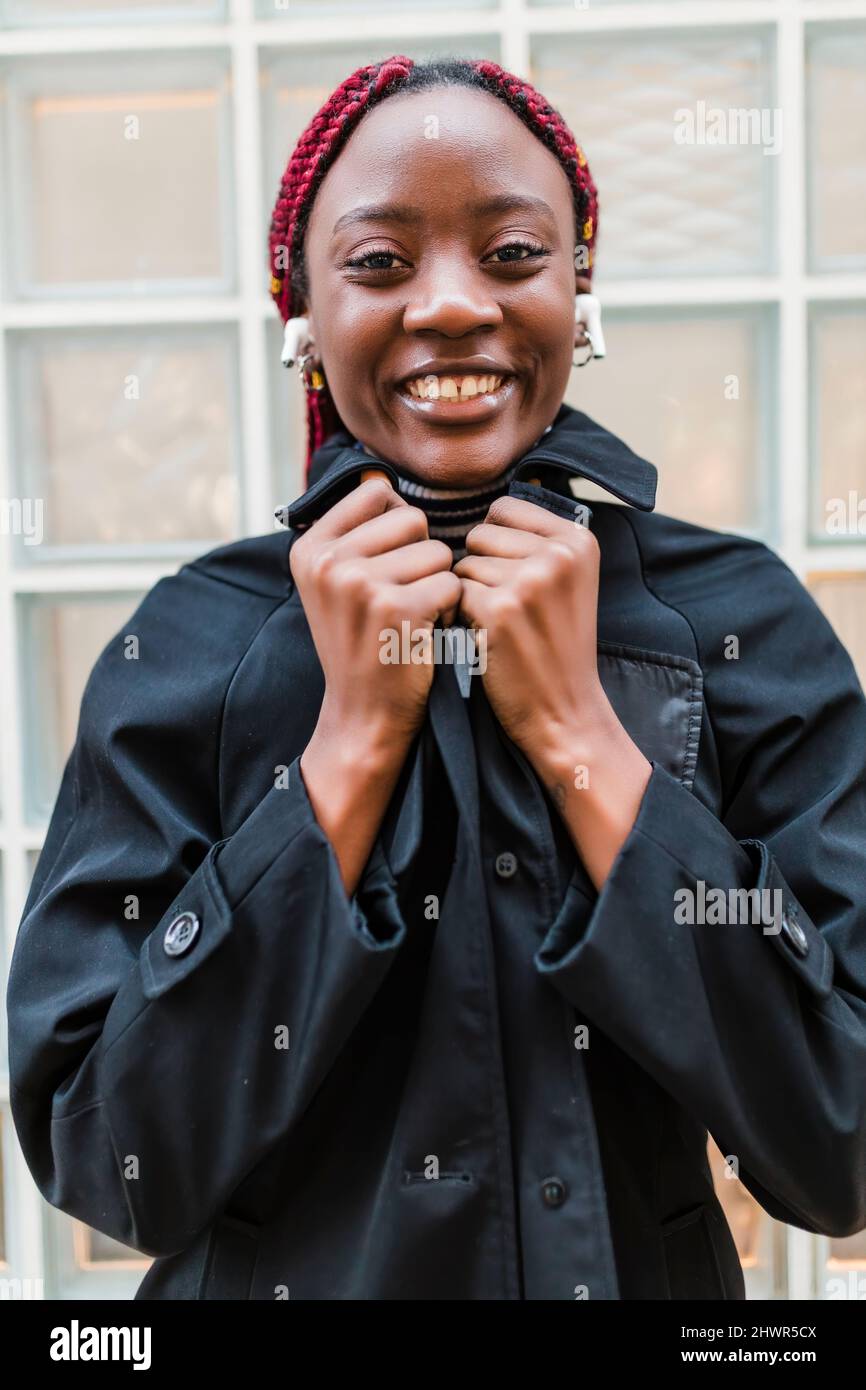 Femme souriante avec écouteurs intra-auriculaires sans fil dans une veste noire Banque D'Images