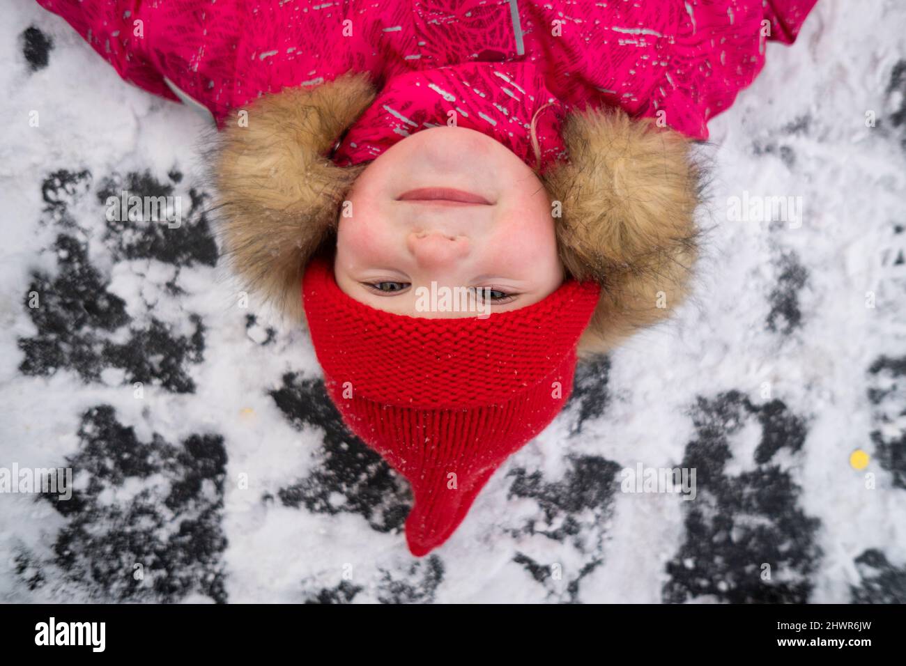 Fille souriante portant un chapeau tricoté rouge couché sur la neige Banque D'Images