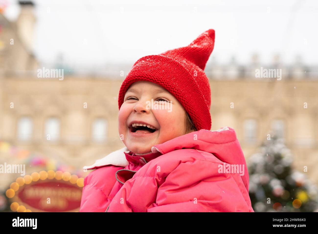 Fille gaie portant un chapeau tricoté rouge appréciant au marché de Noël Banque D'Images