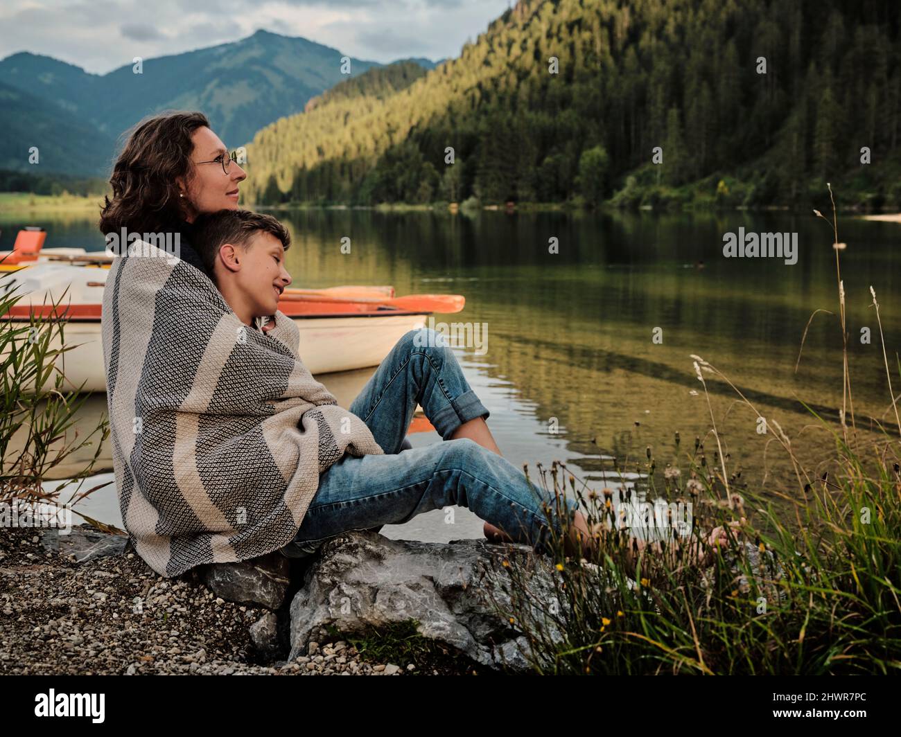 Mère et fils enveloppés dans une couverture assise au bord du lac Banque D'Images