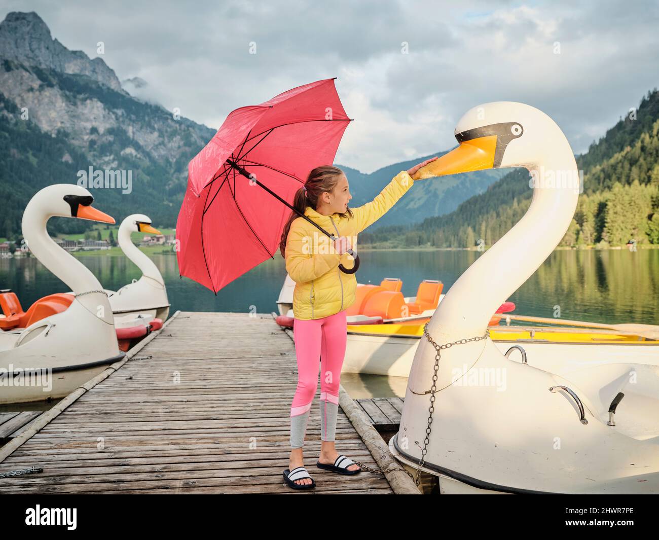 Fille tenant un parapluie rouge touchant le bec de cygne sur la jetée Banque D'Images