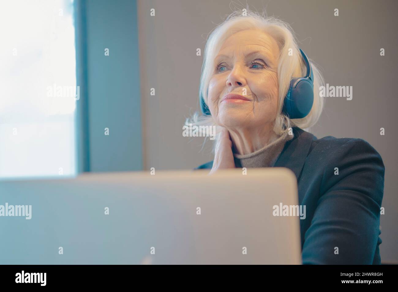 Femme âgée souriante avec ordinateur portable et casque Banque D'Images