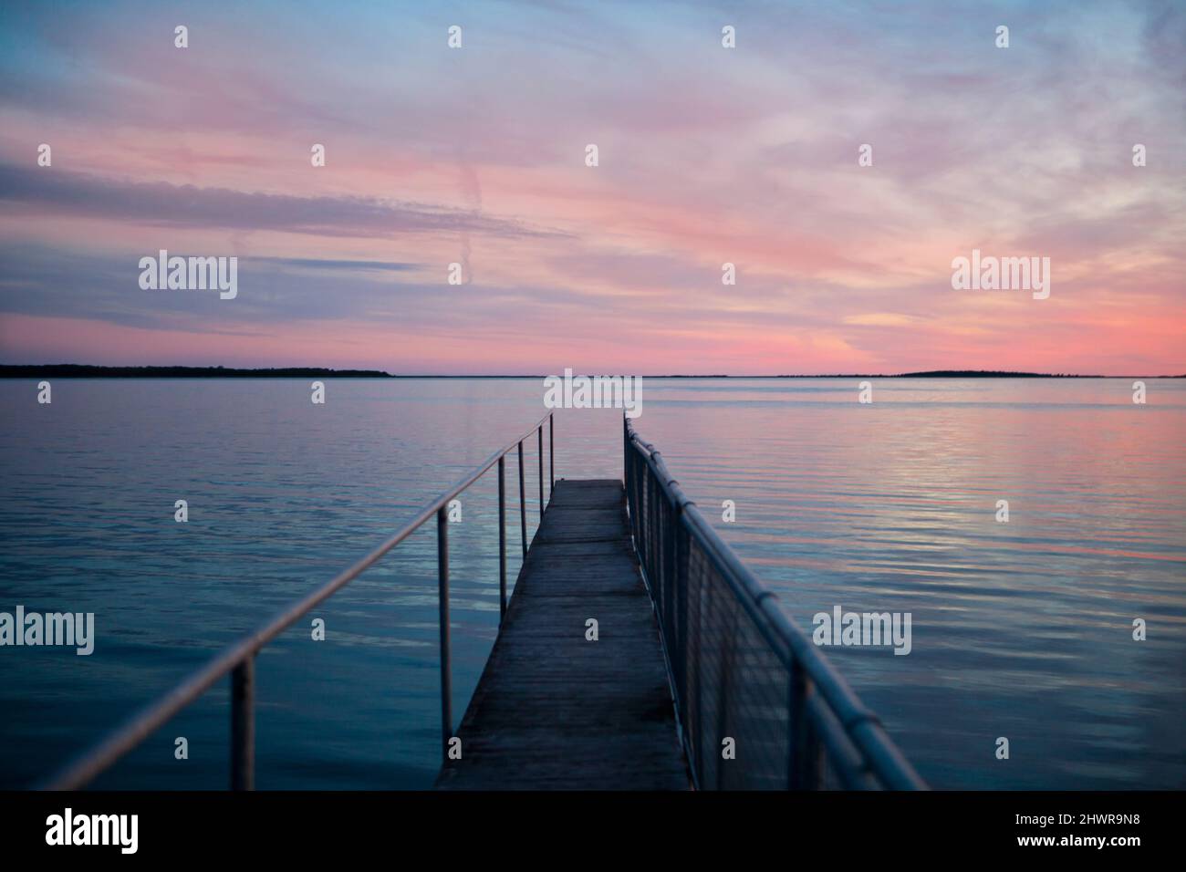 coucher de soleil rose sur la jetée en bois sur la mer bleue. vue sur la longue jetée qui s'étend sur l'océan. réflexion sur l'eau Banque D'Images