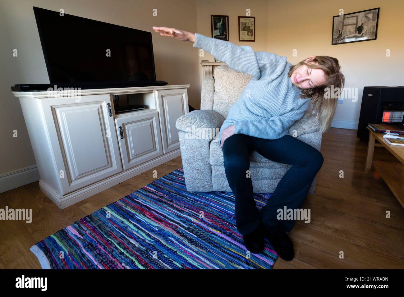 Grande femme blonde faisant des exercices d'étirement matinaux dans un fauteuil Banque D'Images