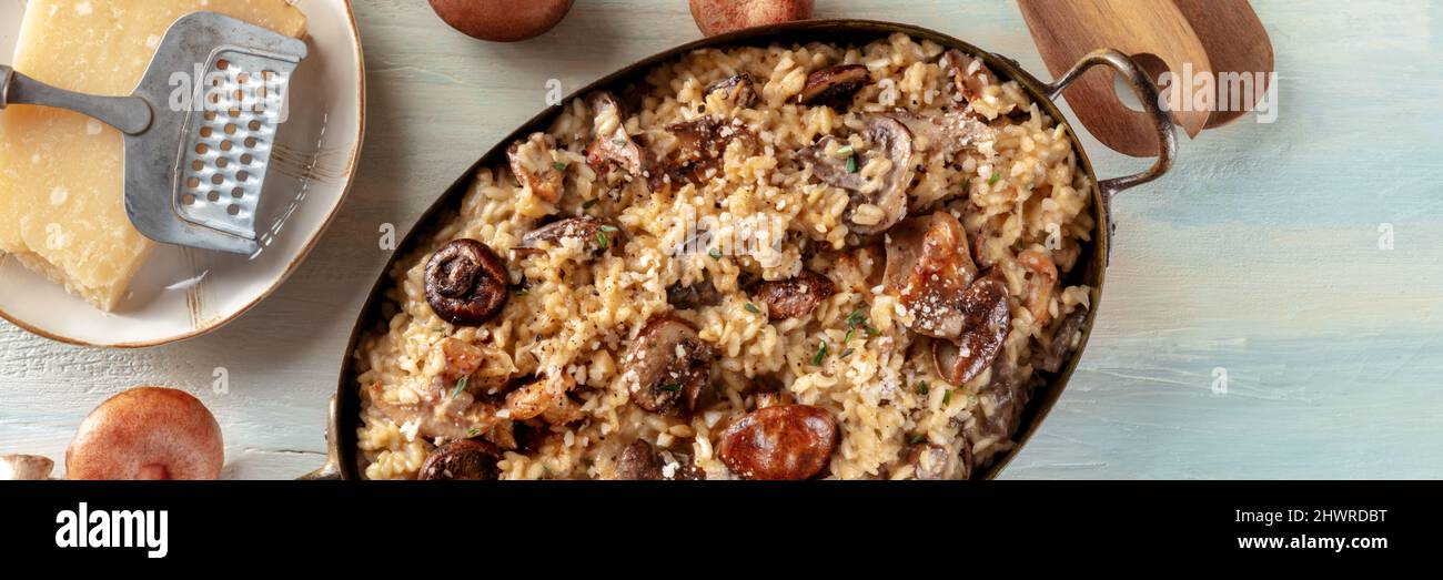 Risotto ai funghi panorama, bannière panoramique de riz aux champignons et au fromage, avec des ingrédients, plan à plat sur fond de bois Banque D'Images